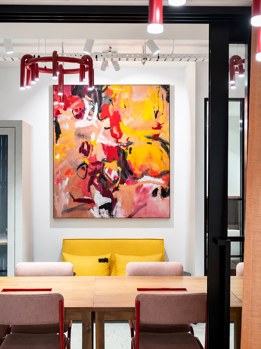 Workshop area with large abstract painting, yellow sofa and red pendant lights