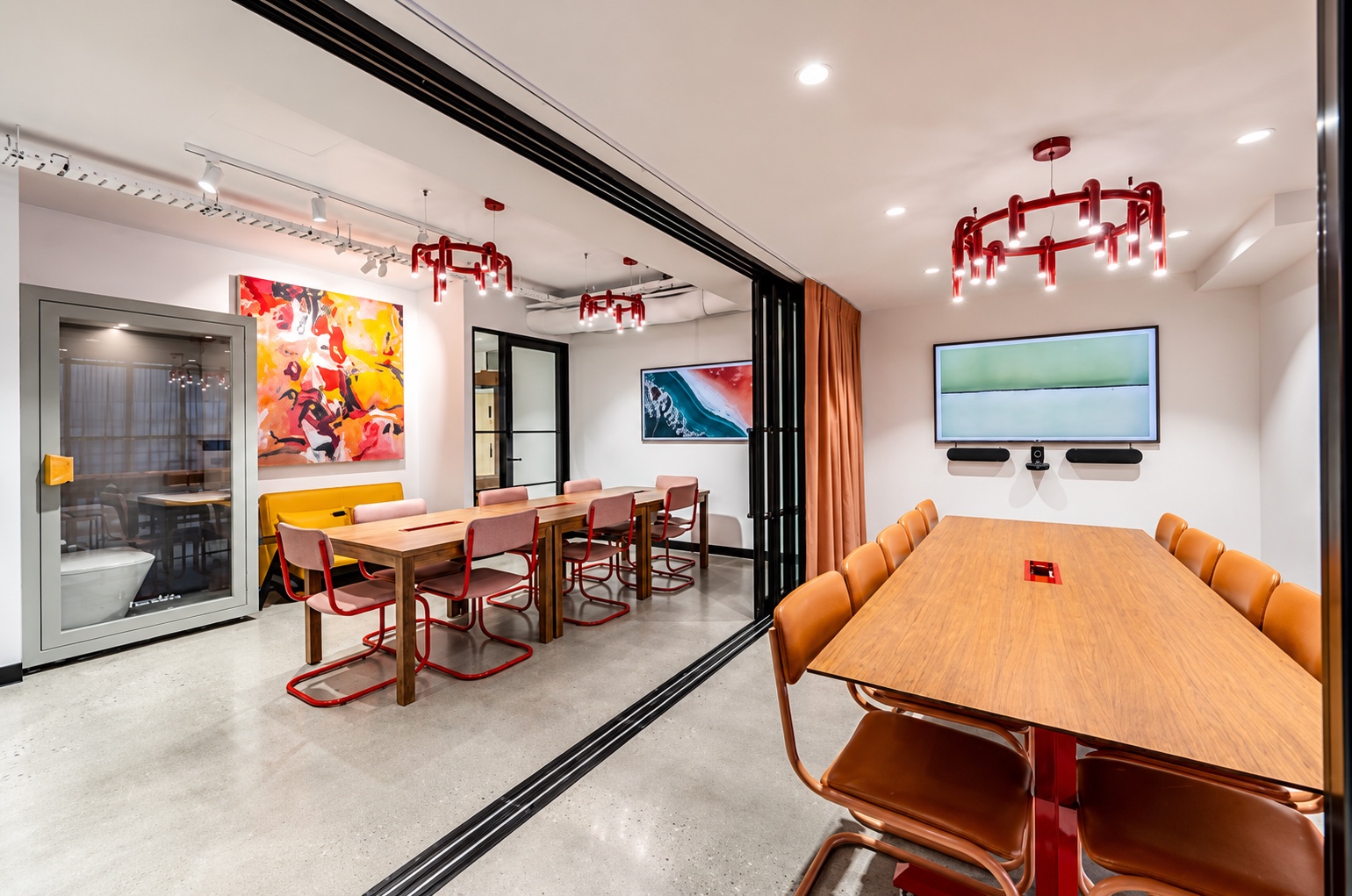 Boardroom and workshop area combined with the glass partition open, timber tables and red pendant lights