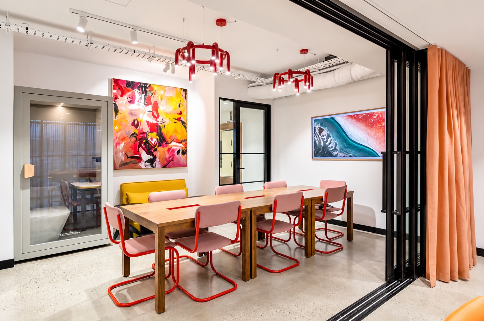 Long timber workshop table with orange chairs under red pendant lights
